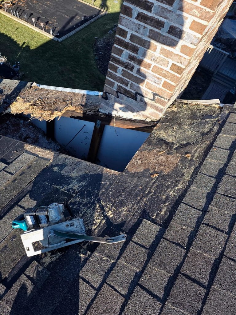Rotted plywood roof deck exposed at chimney showing 15 years of water damage
